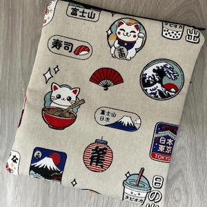 May include: Beige zipped pouch featuring a repeating pattern of Japanese illustrations. The design includes sushi, Mount Fuji, lucky cats, ramen, a fan, a wave, a lantern, and a boba drink. The pouch has a black zip.