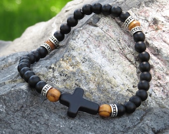 May include: Black onyx bead bracelet with a wooden cross charm and silver accents. The bracelet is on a gray rock background.