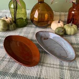 May include: Two oval ceramic serving dishes, one brown and one blue-grey, on a white and grey checkered surface.