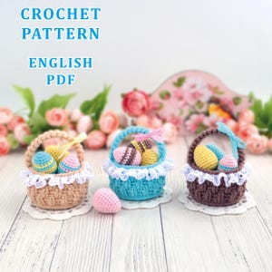 Op de afbeelding: Drie gehaakte paasmandjes in beige, blauw en bruin, elk gevuld met kleurrijke gehaakte eieren. De mandjes hebben witte kanten randen en staan op witte onderzetters. De tekst "CROCHET PATTERN ENGLISH PDF" is inbegrepen.