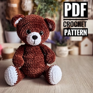 Puede incluir: Un oso de peluche de crochet marrón con patas de crochet blancas. El oso está sentado sobre una superficie de madera. El texto "PDF CROCHET PATTERN" está en el fondo.