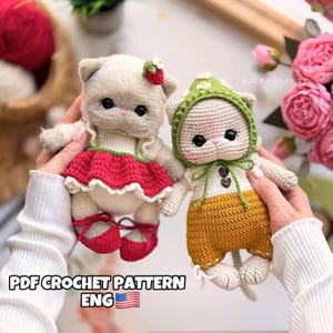 Può includere: Due bambole a forma di gatto all'uncinetto fatte a mano. Un gatto indossa un vestito e scarpe rosse, l'altro indossa un cappello verde e pantaloni gialli. Le bambole hanno gli occhi neri. Il testo "PDF CROCHET PATTERN ENG" è in basso.