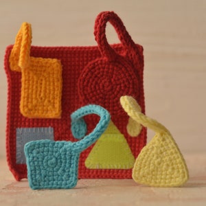 Puede incluir: Un juguete sensorial de crochet con diferentes formas y texturas de colores. El juguete est&aacute; hecho de hilo rojo, naranja, amarillo, verde, azul y gris. Tiene un lazo para colgarlo.
