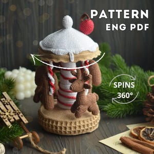 May include: A crocheted carousel with a white roof, brown and white striped pole, and brown reindeer and gingerbread man figures. The carousel is on a woven base. Text on the image reads "PATTERN ENG PDF" and "SPINS 360°."