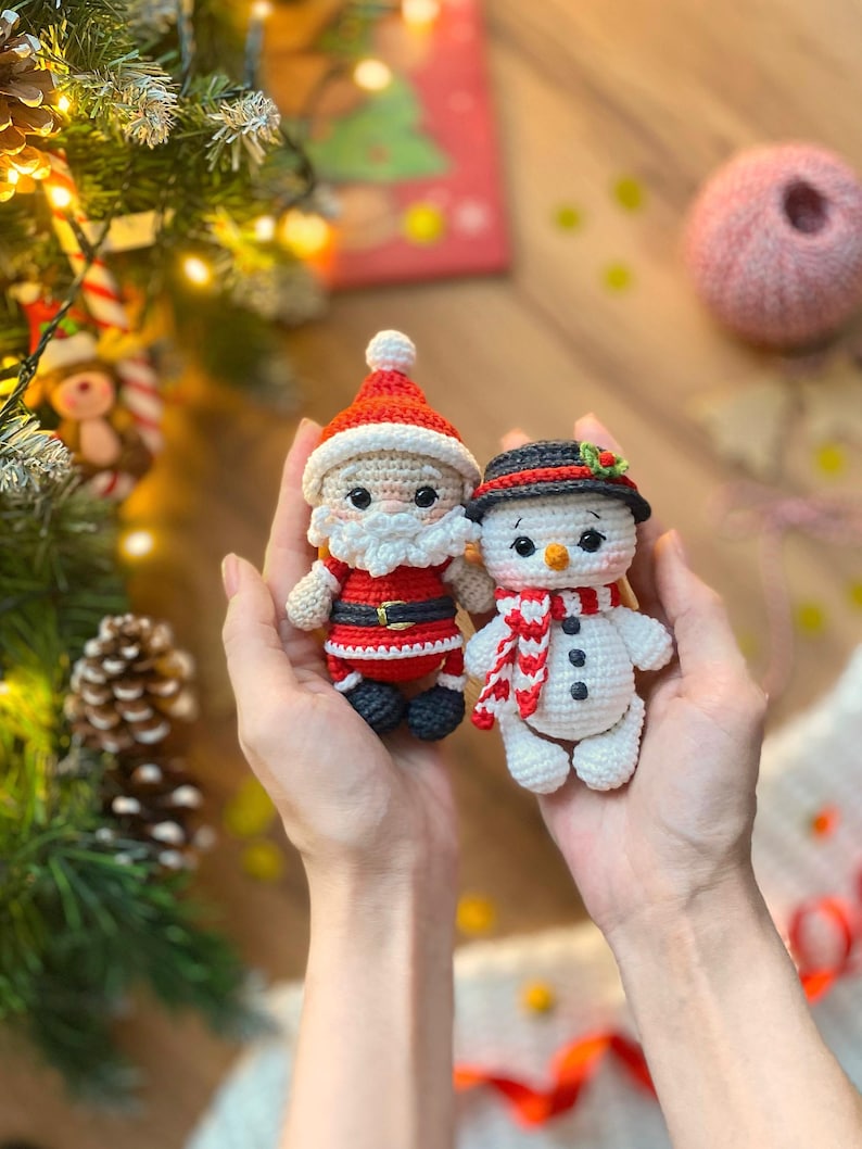 May include: Adorable crocheted Christmas ornaments: a Santa Claus and a snowman. Santa is dressed in a red suit with white trim, and the snowman wears a black hat and red and white striped scarf. Both are crafted with detailed features and charming expressions, perfect for holiday decorations or gifts.