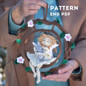 Op de afbeelding: Haakpatroon voor een pop en een konijn die in een schommel van takken en bloemen zitten. Het patroon is beschikbaar in het Engelse PDF-formaat.