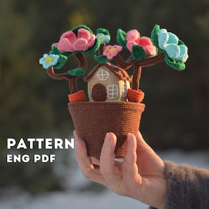Może przedstawiać: Wzór na szydełku do miniaturowego domu z doniczką i kwiatami. Wzór jest dostępny w formacie PDF w języku angielskim.