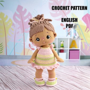 Puede incluir: Patrón de crochet para una muñeca de piel marrón que lleva un vestido a rayas rosa y verde con un dobladillo con volantes. La muñeca tiene el pelo marrón en una coleta y ojos marrones. El patrón está en inglés y está disponible para descargar en PDF. CROCHET PATTERN ENGLISH PDF