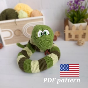 May include: Crochet pattern for a green and brown striped snake amigurumi toy. The snake has large green eyes and a cute expression. The pattern is available as a PDF download. The image also includes a US flag.