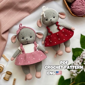 Può includere: Due giocattoli di topo grigi all'uncinetto che indossano abiti rosa e rossi con pois bianchi. I giocattoli sono seduti su una superficie bianca con una coperta rosa e un rocchetto di filo di legno sullo sfondo. Il testo "PDF CROCHET PATTERN ENG" è visibile nell'angolo in basso a destra dell'immagine.