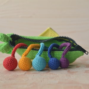 Puede incluir: Una bolsa verde de crochet con cremallera y una gama de bolas de crochet arco&iacute;ris unidas a los tiradores de la cremallera.