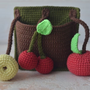 Puede incluir: Un bolsillo de pared de crochet marr&oacute;n con tres cerezas rojas de crochet y una manzana amarilla de crochet. Las cerezas y la manzana tienen hojas verdes de crochet.