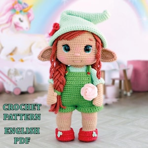 Puede incluir: Patrón de crochet para una muñeca elfo verde con cabello rojo, un sombrero verde y una flor rosa. El patrón está disponible en inglés y es una descarga PDF.