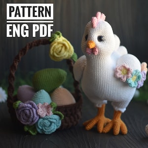 May include: A crocheted white chicken with orange feet and pink accents, holding a brown basket filled with crocheted eggs and flowers. The basket is decorated with crocheted flowers in shades of purple, blue, and green. The image includes the text "PATTERN ENG PDF".