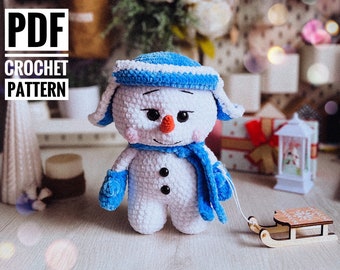 May include: Crochet pattern for a white snowman with a blue hat and scarf. The snowman is holding a small wooden sled.