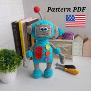 Op de afbeelding: Haakpatroon PDF voor een blauw robot amigurumi speelgoed met kleurrijke knoppen. Het patroon bevat instructies voor het maken van de robot en zijn accessoires. Het patroon is beschikbaar in Amerikaans Engels.