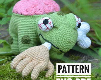 May include: Crochet pattern for a green zombie with a pink brain, one arm, and a bone in its mouth. The pattern is in English and is available as a PDF download.  PATTERN ENG PDF