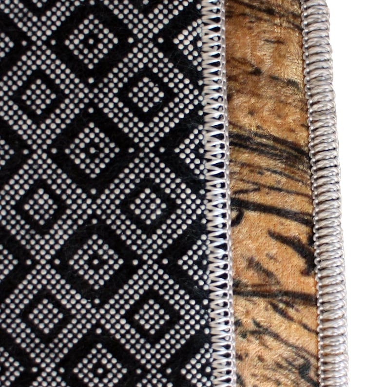 May include: Close-up of a rug with a black and white geometric pattern on the left and a tiger stripe pattern on the right. The edges are trimmed with a silver-colored, stitched border. The rug has a soft, plush texture.