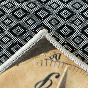 May include: A corner of a beige, circular patch with a white stitched border, featuring a partial view of a black and white patterned fabric. The patch has a vintage aesthetic, with visible text and the number "50".