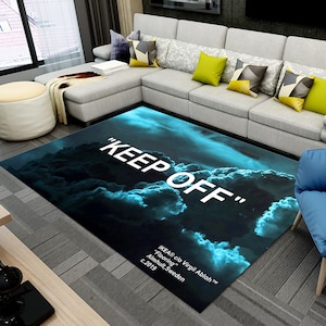 Può includere: Un tappeto blu e nero con un design a nuvole bianche e la scritta "KEEP OFF" stampata su di esso. Il tappeto include anche il testo "IKEA® c/o Virgil Abloh™" e "Flooring" in bianco.