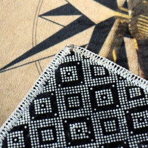 May include: Close-up of a black and white patterned fabric with a white stitched border. The fabric has a geometric design with small white dots.