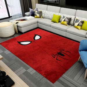May include: A rectangular red rug featuring a Spider-Man design. The rug displays the character's mask with white eyes and a black spider emblem. The rug is placed on a gray floor in a living room setting.