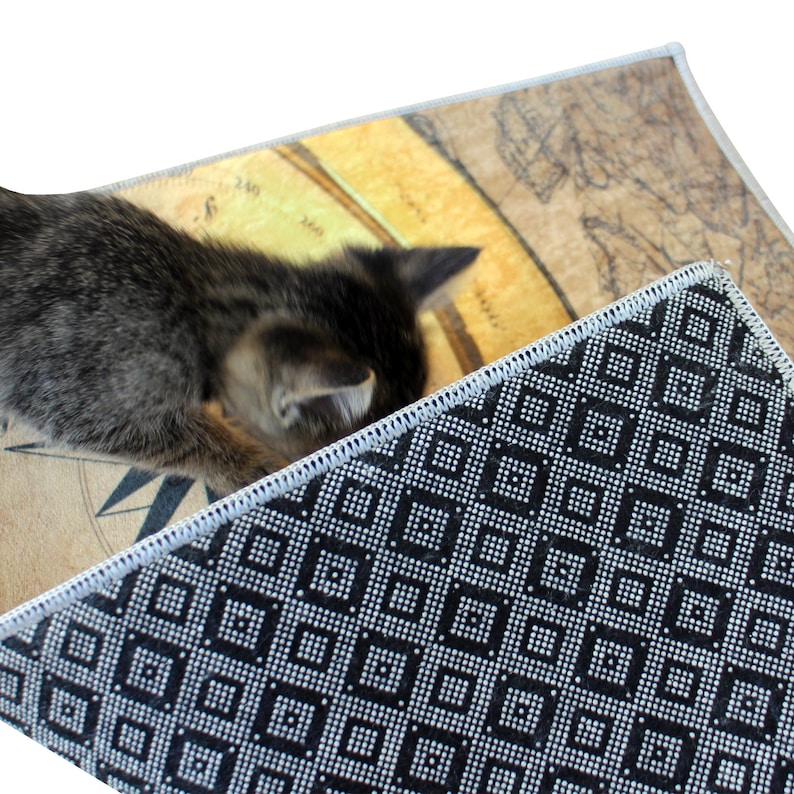 May include: A close-up of a black and white patterned rug with a gray kitten lying on top of it. The rug has a geometric pattern of squares and dots. The kitten is looking down at the rug.