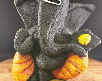 Op de afbeelding: Zwart Ganesha-beeld met een rode stip op zijn voorhoofd en een geel-oranje geverfde basis.