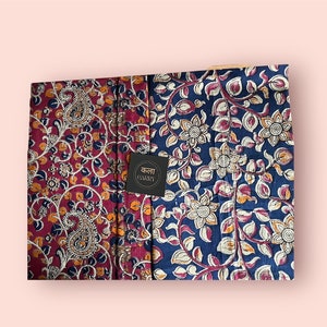 May include: Two fabric pieces with detailed floral and paisley patterns. One is a deep burgundy with a paisley design, and the other is navy blue with a floral pattern. A black tag with the text "Kala Carry" is in the centre.