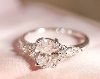 Peut inclure: Une bague de fiançailles en argent avec un grand diamant de forme ovale et des diamants plus petits sur la bande. La bague est posée sur un coussin de velours rose.