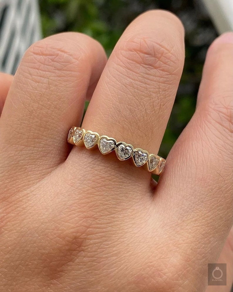 K&ouml;nnte beinhalten: Ein Goldring mit einer Reihe herzf&ouml;rmiger Diamanten. Der Ring befindet sich an einem Finger.