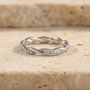 Peut inclure: Une bague argentée présentant un design de bande torsadée et tressée. L'un des brins du métal torsadé est incrusté de petites pierres claires et scintillantes qui captent la lumière, tandis que l'autre brin reste lisse et poli.