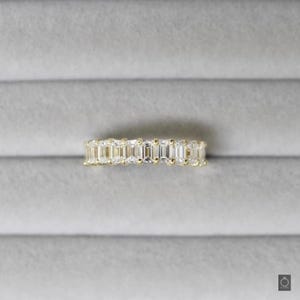 May include: A gold band ring with a row of emerald-cut diamonds.