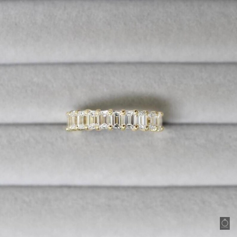 May include: A gold band ring with a row of emerald-cut diamonds.
