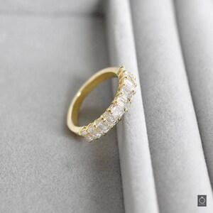 May include: A gold band ring with a row of clear, rectangular-shaped stones.