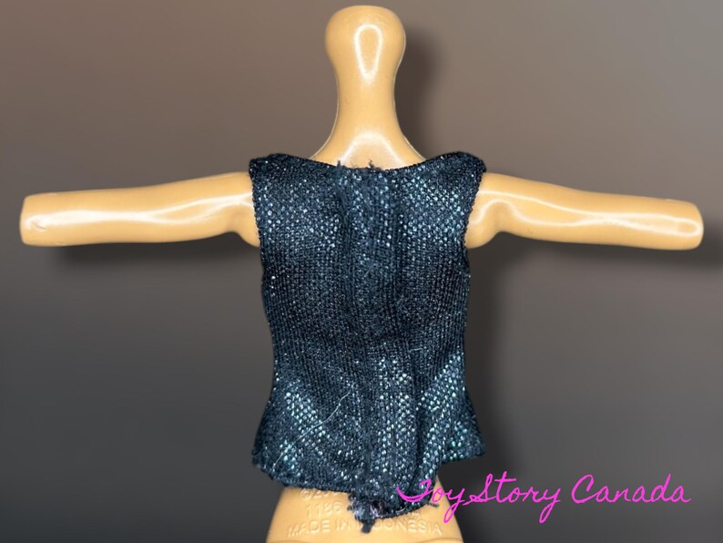 Puede incluir: Una blusa sin mangas de color azul oscuro con una tela texturizada y brillante. La blusa se muestra en un maniqu&iacute; con los brazos extendidos. La parte inferior de la blusa tiene un ligero volante.