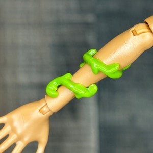 Puede incluir: Un brazo de muñeca con una sustancia viscosa verde envuelta alrededor.