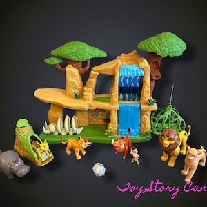Puede incluir: Un set de juego de plástico de El Rey León con una formación rocosa color canela, una cascada azul, árboles verdes y una base verde. Incluye figuras de plástico de un león, una leona, un cachorro, un jabalí, un suricato, un hipopótamo y una jaula.