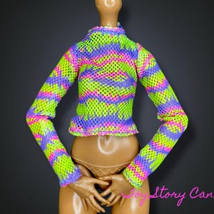 Puede incluir: Una camiseta de malla de manga larga de color neón, con un vibrante estampado en verde, rosa y morado. La camiseta tiene un cuello alto y un dobladillo con volantes. La prenda se exhibe en un maniquí.
