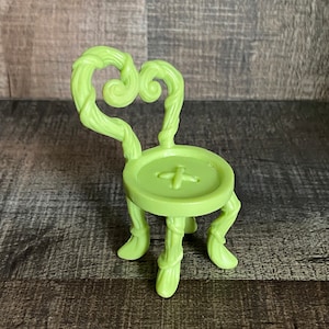 Könnte beinhalten: Ein limettengrüner Plastikstuhl mit einem einzigartigen Design. Der Stuhl hat eine herzförmige Rückenlehne und drei Beine, die an Ranken erinnern. Die Sitzfläche ist rund und hat in der Mitte ein knopfähnliches Design.