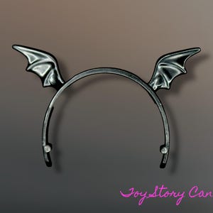May include: A black bat wing headband. The wings have a textured, metallic appearance. The headband is a curved design, with small, clear embellishments at the ends. A Halloween costume accessory.