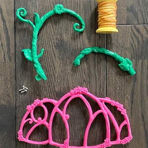 Puede incluir: Un kit de casa de hadas de plástico rosa con enredaderas de plástico verde, un carrete de cuerda marrón y dos tornillos pequeños.