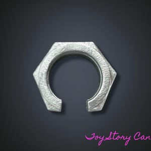 Può includere: Un anello esagonale color argento con una superficie strutturata e un'apertura circolare. L'anello ha una spaccatura nella parte inferiore. Lo sfondo è grigio scuro.