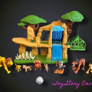 Puede incluir: Un juego de plástico que presenta una formación rocosa de color tostado con una cascada azul, dos árboles verdes y una jaula verde colgante. Se incluyen varias figuras de animales pequeños, como un león, un jabalí, un mono y un leopardo.