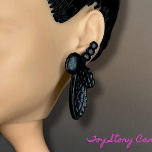 Pode incluir: Brincos pendentes pretos com um design floral texturizado. Os brincos são feitos de um material leve e têm um visual delicado e feminino.