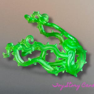 Peut inclure: Un élément décoratif translucide vert vif en forme de vigne avec des épines. La pièce en plastique a une forme organique incurvée, avec de multiples vrilles et de petites protubérances pointues. L'objet est posé sur un fond neutre.