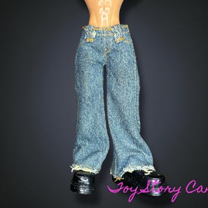 Pode incluir: Jeans de ganga azul clara para bonecas, com bainhas desfiadas. Os jeans são combinados com sapatos pretos. A imagem é definida contra um fundo escuro.
