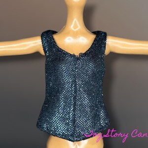 Puede incluir: Un top azul oscuro con lentejuelas y cuello en V. El top tiene una silueta ajustada y est&aacute; dise&ntilde;ado para ser usado en una mu&ntilde;eca. La tela tiene una apariencia texturizada y brillante.