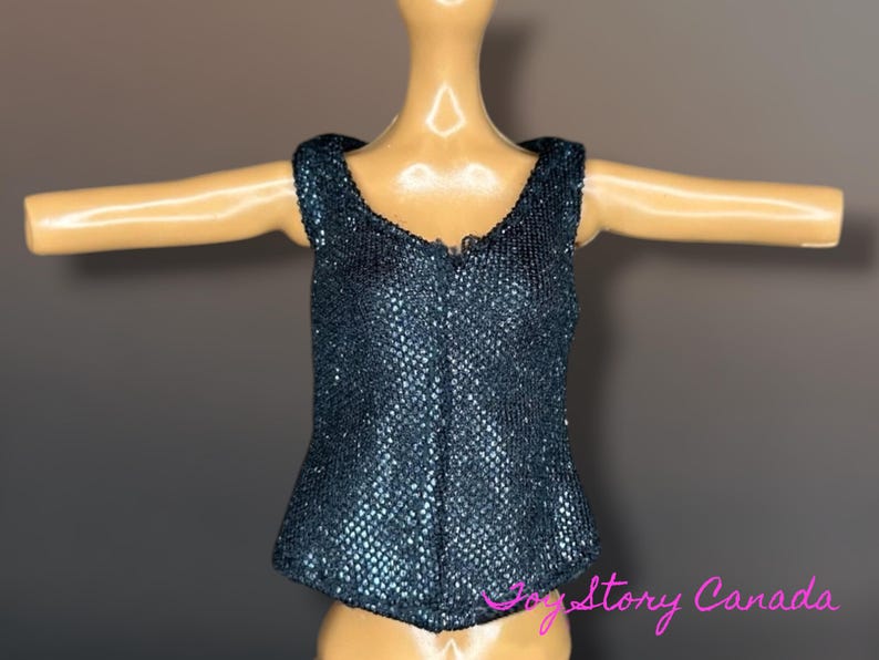 Puede incluir: Un top azul oscuro con lentejuelas y cuello en V. El top tiene una silueta ajustada y est&aacute; dise&ntilde;ado para ser usado en una mu&ntilde;eca. La tela tiene una apariencia texturizada y brillante.