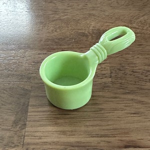 May include: A small, light green plastic measuring scoop with a handle shaped like a twisted rope.